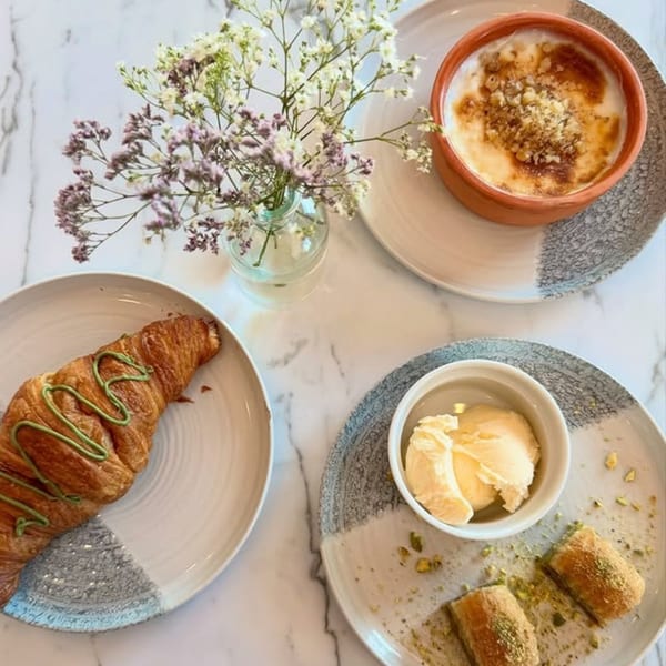 A croissant, rice pudding, baklava, and ice cream on a marble table with a small vase of flowers.