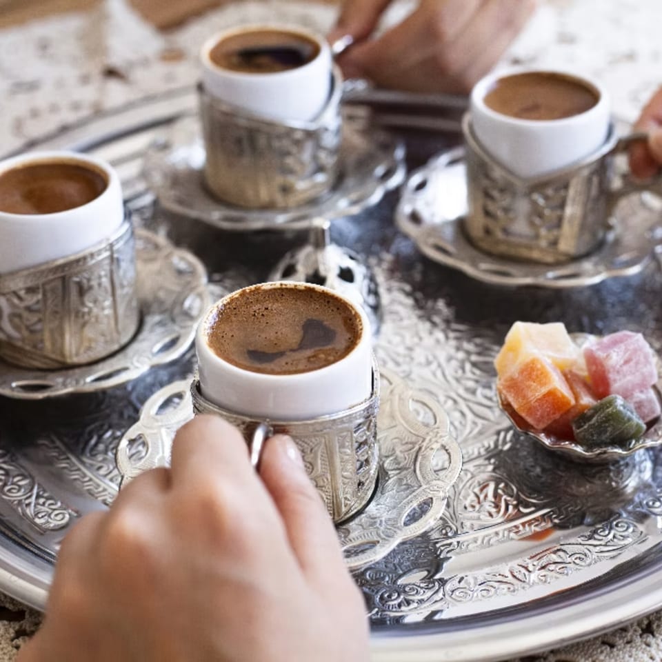 Four cups of Turkish coffee in ornate silver holders on a tray with colorful Turkish delight.